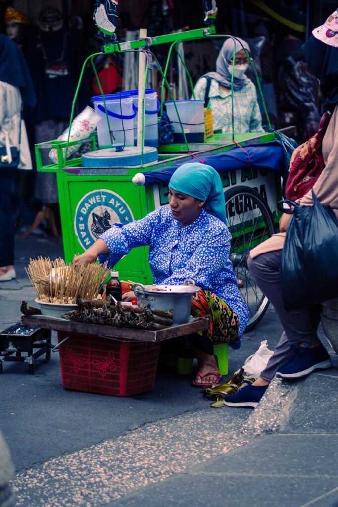 A woman street vendor selling traditional snacks on a vibrant street in Yogyakarta, Indonesia.