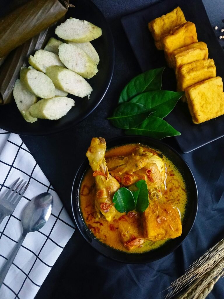Delicious Indonesian opor ayam served with rice cakes and tofu, presented on a dark background.